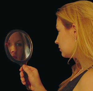 Woman gazes in mirror.