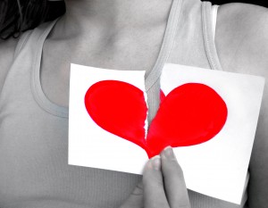black and white close up photo of woman holding ripped piece of paper with bright red heart on it