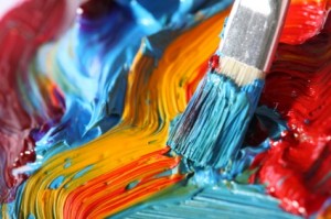 close up of paintbrush adding blue paint to a multicolored abstract painting