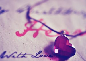 close up of red crystal heart necklace on paper with cursive writing that says Heart and With Love