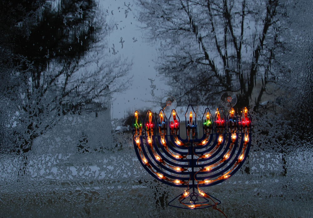 lit up menorah in windowsill showing snowy evening outside