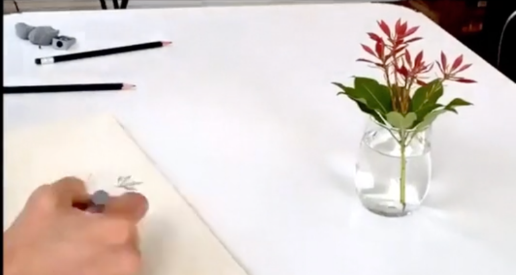 hand writing on paper on a white table with pencils and a pink flower in a small vase