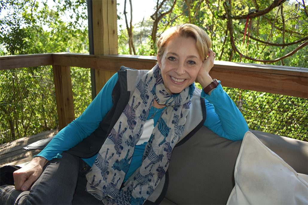 Martha Beck sitting on outdoor patio leaning head on hand smiling at camera