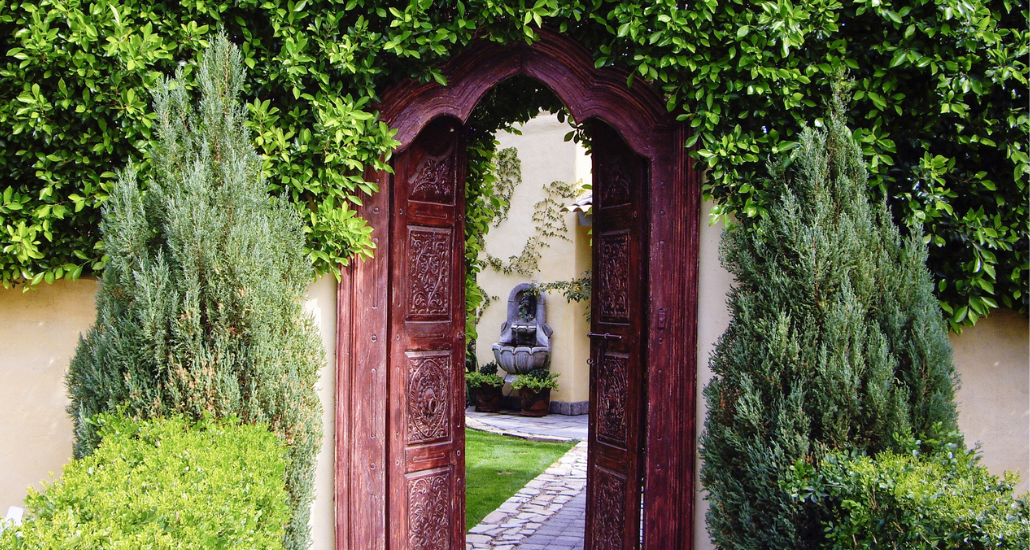 An elaborate carved wood door surrounded by greenery leading into a secret garden.