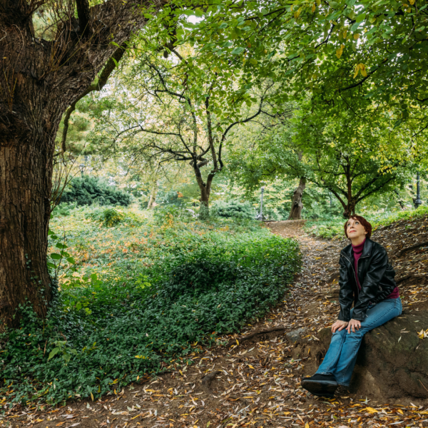 Martha sitting on a large rock looking reflective underneath a canopy of green leaves.
