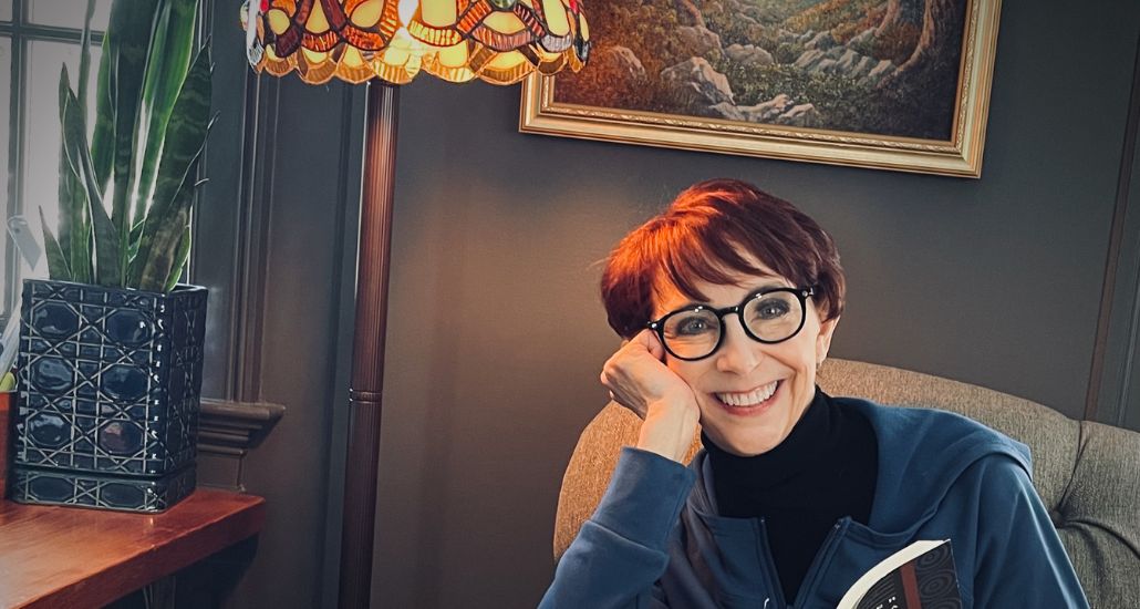 Martha smiling in front of a painting, holding an open book.