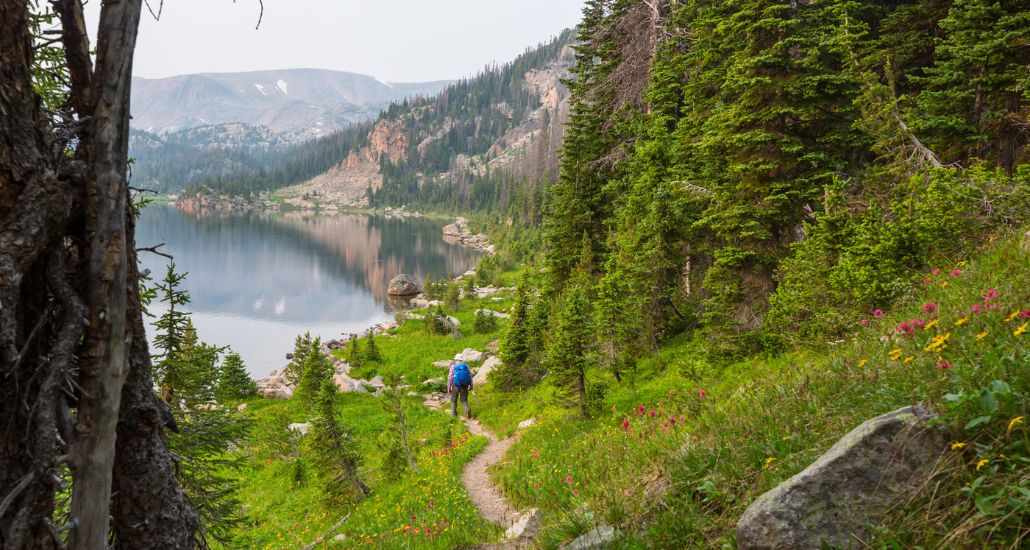 person hiking on a mountain path leading to a lak